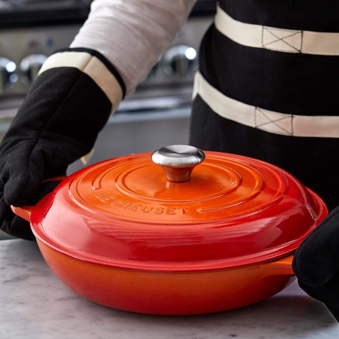 Roter Bräter auf Marmortisch mit Handschuhen.