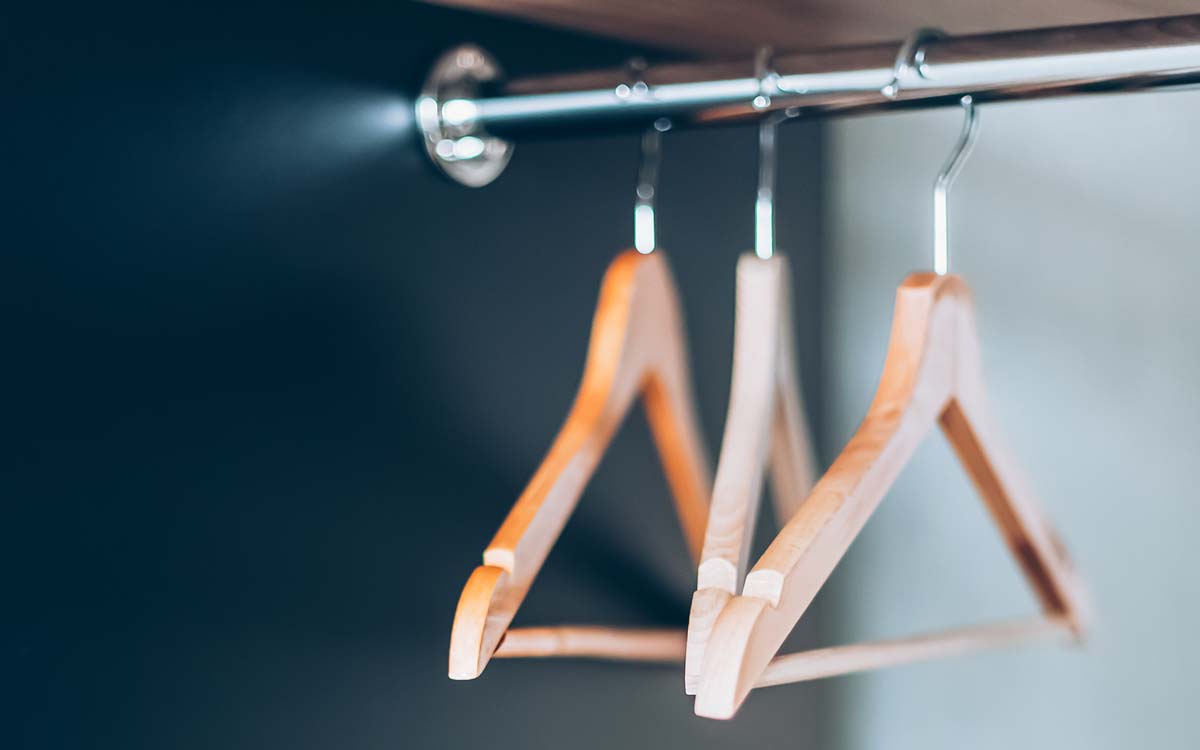 Drei Holzkleiderbügel an einer Stange.