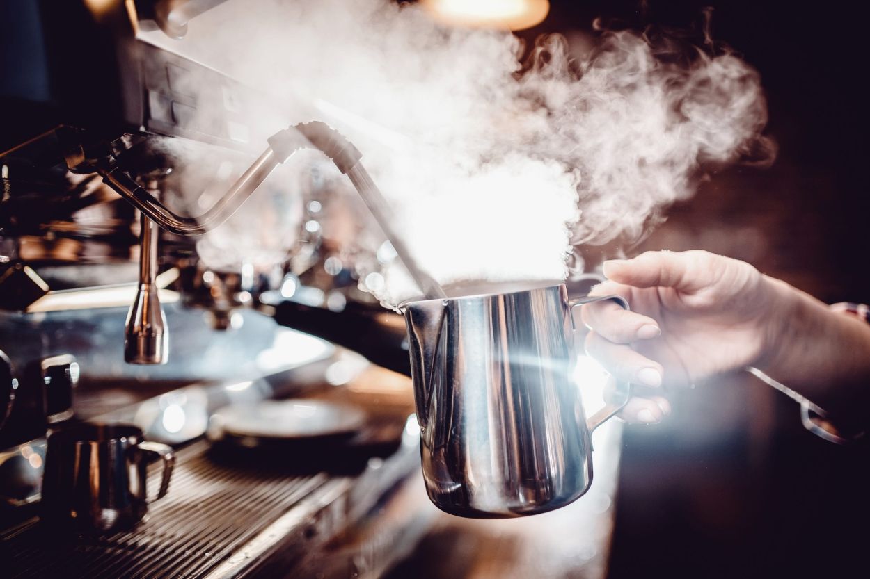 Dampfdüse schäumt Milch in Edelstahlkanne auf.