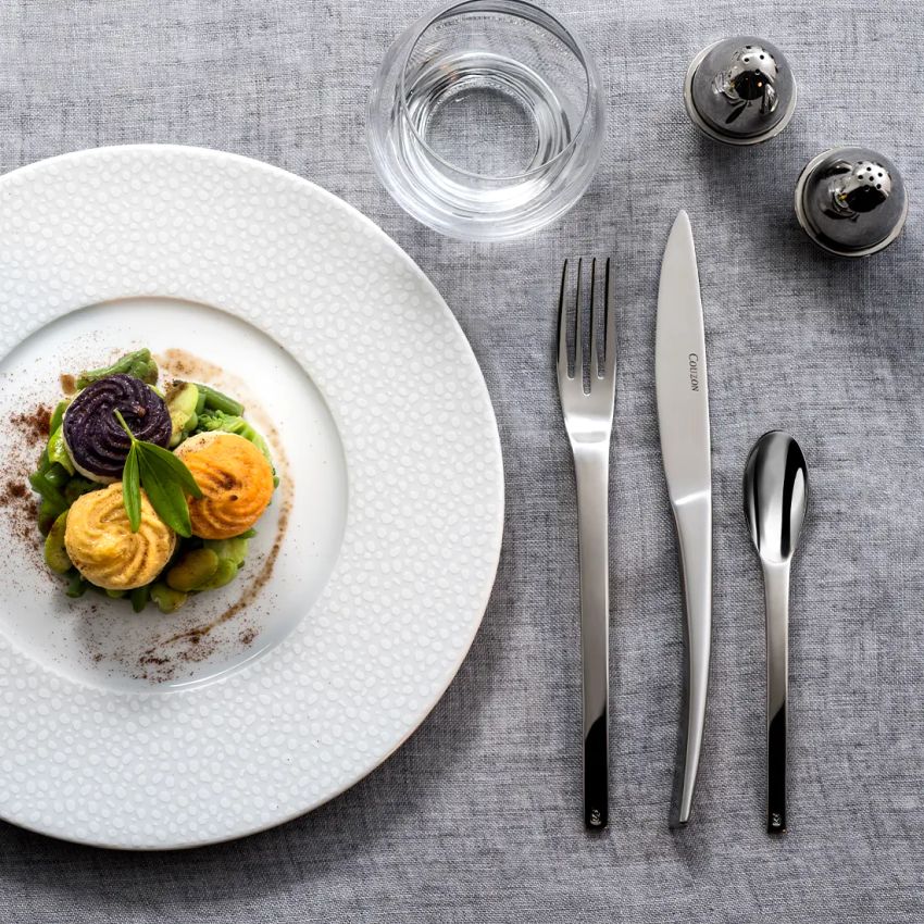 Teller mit Besteck und Glas auf Tischdecke.